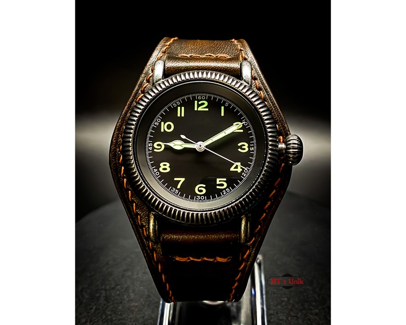 May include: A black watch with a brown leather strap and a black face with white numerals. The watch has a luminous dial with a white second hand.