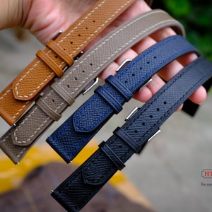 Peut inclure: Quatre bracelets de montre de différentes couleurs, dont le marron, le gris, le bleu et le noir. Les bracelets sont en cuir et présentent un design cousu. Les bracelets sont disposés en pile, le bracelet marron en haut et le bracelet noir en bas.