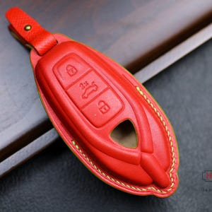 May include: Red leather key fob with gold stitching. The fob has three buttons with symbols for lock, unlock, and trunk release.