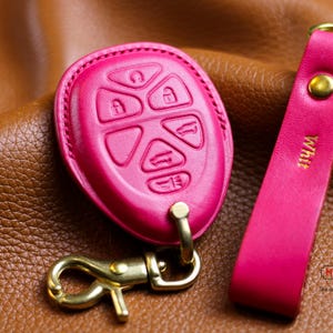 May include: A pink leather key fob with a gold metal key ring and a matching pink leather strap. The strap has the word "White" embossed on it.