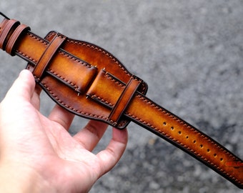 May include: A brown leather watch band with a buckle and stitching. The band is designed to fit around the wrist.