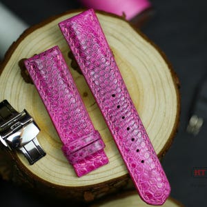 Op de afbeelding: Felroze horlogeband met een getextureerd, reptielachtig patroon. De band wordt in twee delen getoond, met een zilveren sluiting en een houten achtergrond. De band is ongeveer 20 cm lang.