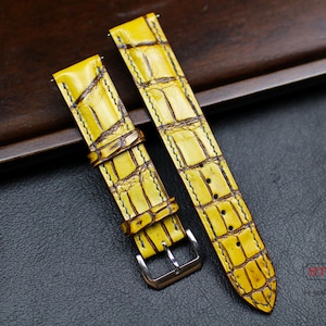 May include: Two yellow leather watch straps with a crocodile pattern. The straps are stitched with a dark thread and have a buckle on one end.