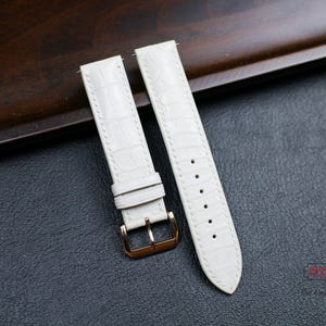 May include: Two white leather watch straps with gold buckles. The straps have a crocodile pattern.