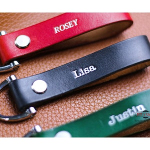 Può includere: Tre portachiavi in ​​pelle con anelli argentati. I portachiavi sono rosso, nero e verde. I nomi "Rosey", "Lisa" e "Justin" sono incisi sui portachiavi.