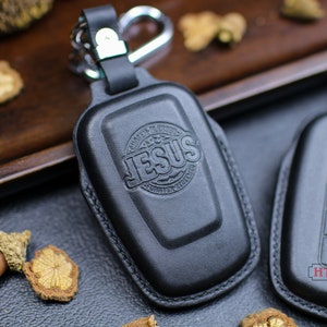May include: Two black leather key covers with a silver metal ring. One cover has the word "JESUS" embossed in a circle. The other cover has a car key with buttons.