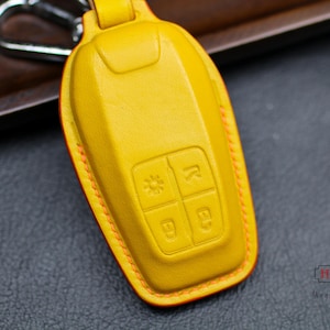 May include: A yellow leather key fob with orange stitching. The fob has four buttons with raised lettering.