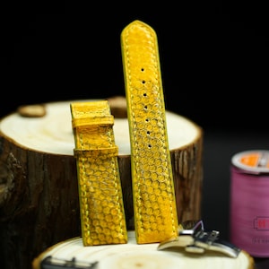 May include: Two yellow leather watch straps with a textured pattern. The straps are on a wooden surface.