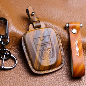 May include: A brown leather key fob with a wood grain pattern and the text "Huckleberry" embossed on the side. The fob is designed to protect a car key.