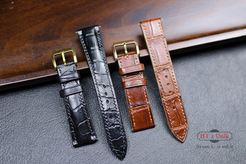 May include: Four different watch straps made of leather with alligator pattern. The straps are in black, brown, and tan colors. The straps have gold buckles.
