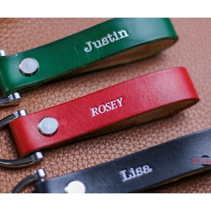 May include: Three leather keychains with silver key rings. The keychains are green, red, and black. The names "Justin", "Rosey", and "Lisa" are embossed on the keychains.