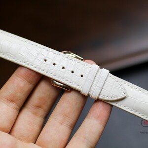 May include: A white leather watch strap with a crocodile pattern.