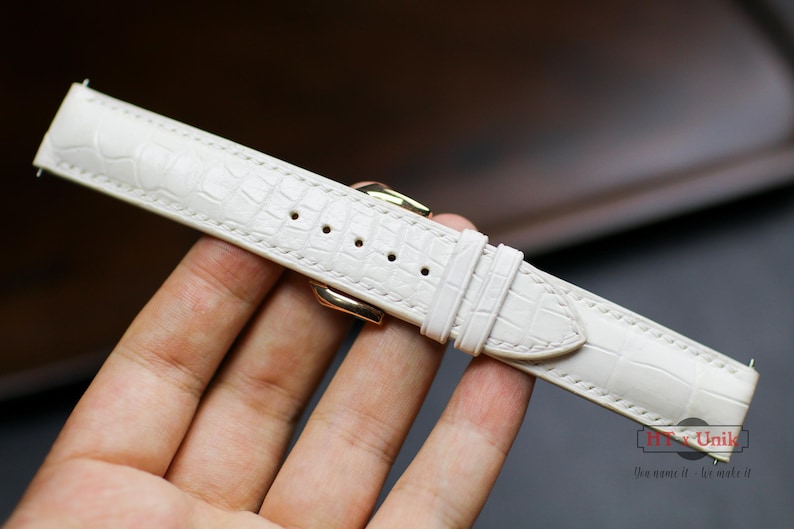 May include: A white leather watch strap with a crocodile pattern.