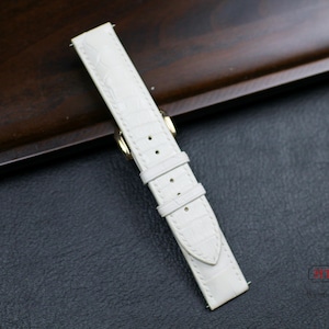 May include: White leather watch strap with a crocodile pattern and gold hardware.