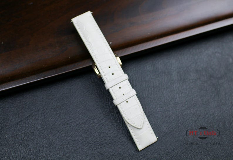 May include: White leather watch strap with a crocodile pattern and gold hardware.