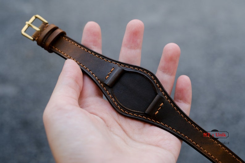 May include: A brown leather watch strap with orange stitching. The strap is designed to fit a watch with a round face.
