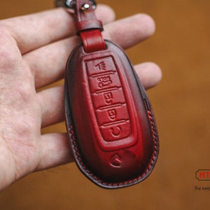 Könnte beinhalten: Roter Leder-Schlüsselanhänger mit einem genähten Rand und fünf Knöpfen. Der Schlüsselanhänger wird in einer Hand gehalten.