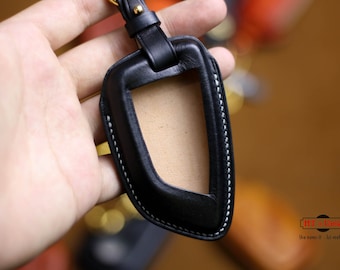May include: Black leather key fob with a white stitching detail and a clear window for a car key. The fob has a gold metal loop for attaching to a keychain.