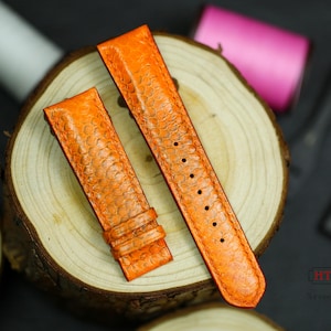 Peut inclure: Deux bracelets de montre en cuir orange avec un motif texturé. Les bracelets sont sur une surface en bois.