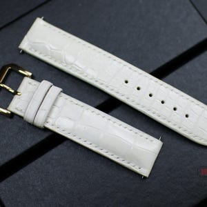 May include: Two white leather watch straps with a crocodile pattern. One strap has a gold buckle.