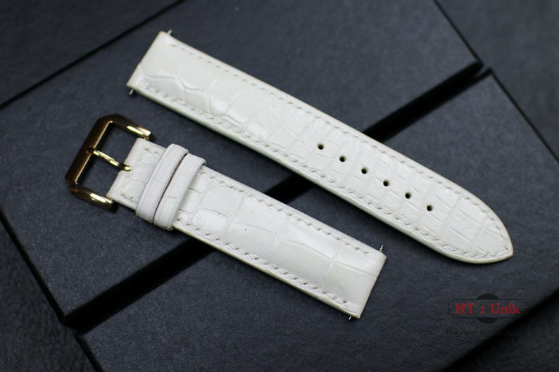May include: Two white leather watch straps with a crocodile pattern. One strap has a gold buckle.