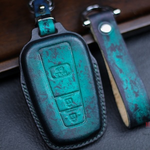 May include: A teal blue leather key fob with a stitched edge and a matching teal blue leather strap with a silver metal ring. The key fob has three buttons.