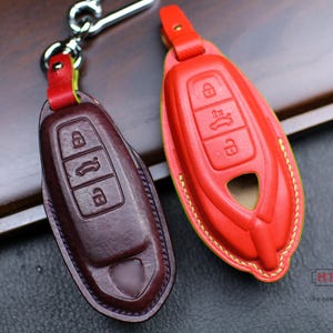 May include: Two leather key covers, one red and one brown, with stitching around the edges. The red key cover has a key fob with three buttons. The brown key cover has a key fob with three buttons. The text "HT x Unik" is visible in the bottom right corner of the image.