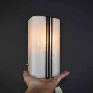 May include: A white frosted glass lamp with black vertical stripes. The lamp is lit and has a warm glow.