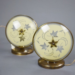 Może przedstawiać: Para vintage stołowych lamp z mosiądzu z kremowym kloszem ze szklanym wzorem srebrnych liści. Lampy mają okrągłą podstawę i przezroczysty szklany klosz.