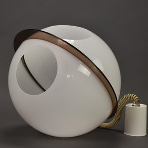 Puede incluir: Una lámpara colgante esférica blanca con una abertura circular. Una banda marrón y negra rodea la esfera. Un cable en espiral color crema se conecta a una base cilíndrica blanca. La lámpara es de diseño moderno.