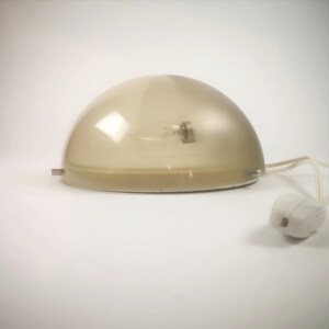 May include: A white dome-shaped lamp with a clear glass shade and a white cord. The lamp is on a white surface.