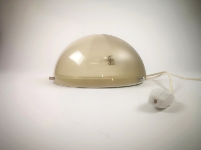 May include: A white dome-shaped lamp with a clear glass shade and a white cord. The lamp is on a white surface.