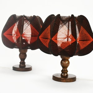 May include: Two vintage table lamps with dark brown wooden bases and shades. The shades are constructed with black and red thread, creating a geometric pattern. The lamps have a classic, mid-century modern design.