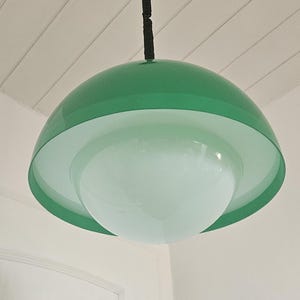 May include: A green and white pendant light fixture. The light has a rounded, layered design with a glossy green outer shade and a white inner shade. The fixture hangs from a black cord and ceiling mount.