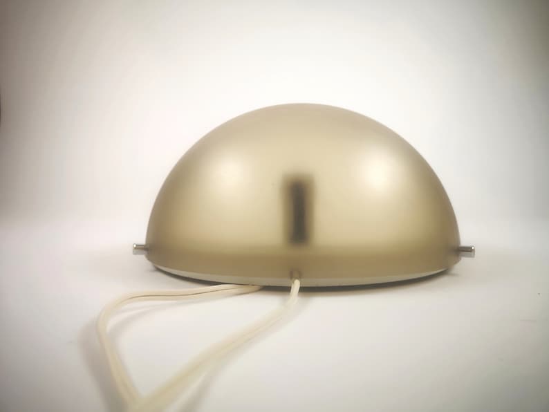 May include: A beige frosted glass dome lamp with a white cord. The lamp has a silver metal base and two silver metal attachments on the side.