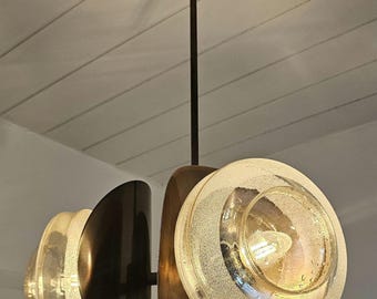 May include: A contemporary pendant light with a dark bronze finish. It features frosted glass globes and curved metal shades in bronze and black. The light hangs from a dark bronze rod.