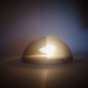 May include: A white and gray dome-shaped lamp with a light bulb inside. The lamp is on a white surface.