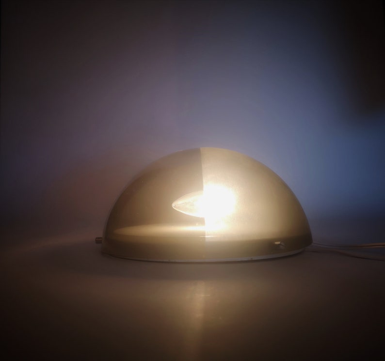 May include: A white and gray dome-shaped lamp with a light bulb inside. The lamp is on a white surface.