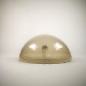 May include: A beige, dome-shaped lampshade with a light bulb inside. The lampshade is made of translucent plastic and has a smooth, rounded surface.