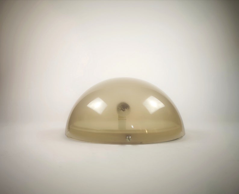 May include: A beige, dome-shaped lampshade with a light bulb inside. The lampshade is made of translucent plastic and has a smooth, rounded surface.