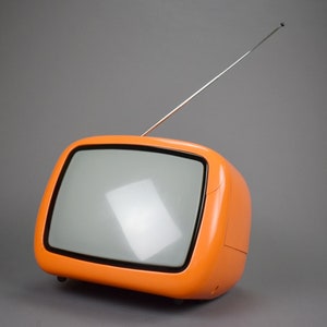 May include: An orange vintage television set with a silver antenna. The TV has a rounded, retro design with a rectangular screen. The television is set against a gray background.