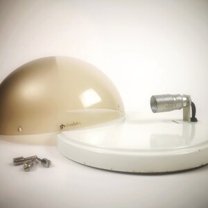 May include: A white and beige modern lamp with a round, translucent shade and a metal arm with a coiled cord. The lamp is disassembled and the parts are laid out on a white surface.