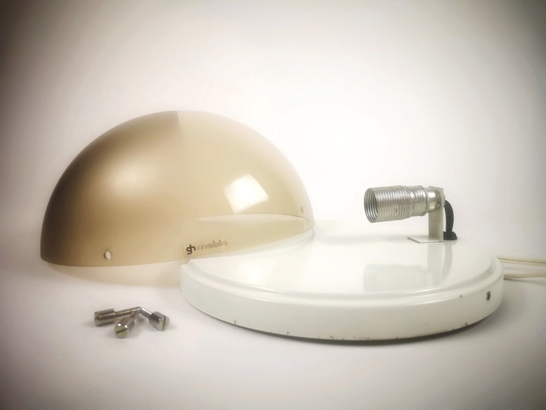 May include: A white and beige modern lamp with a round, translucent shade and a metal arm with a coiled cord. The lamp is disassembled and the parts are laid out on a white surface.