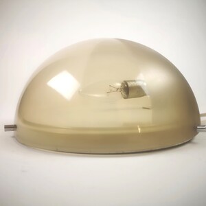 May include: A beige frosted glass dome lampshade with a light bulb inside. The lampshade is on a white surface.