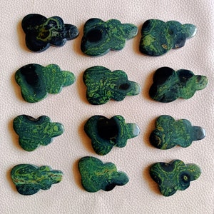 May include: Twelve cloud-shaped stones with a dark green and black marbled pattern. The stones are polished and have a smooth surface. The cloud stones are arranged on a light pink surface.