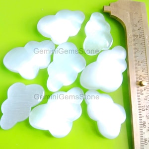 May include: Eight white, cloud-shaped, gemstone cabochons. The cabochons are approximately 1 inch in diameter. A ruler is in the background for size reference.