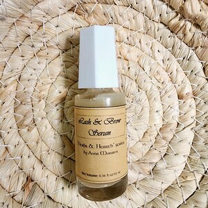 Puede incluir: Una peque&ntilde;a botella de vidrio de suero Lash & Brow con tapa blanca. La etiqueta marr&oacute;n tiene texto negro: "Herbs & Icarth series by Anna Morwen". El volumen neto es de 10 ml.