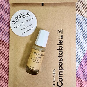 Puede incluir: Una peque&ntilde;a botella de vidrio de suero para pesta&ntilde;as y cejas con una tapa blanca se encuentra sobre un sobre de papel marr&oacute;n. El sobre tiene la palabra "Compostable" impresa. Tambi&eacute;n hay una pegatina redonda con las palabras "Herbs & Hearth".