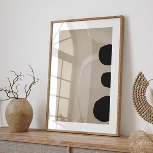 May include: A framed abstract art print with a beige background and three black circles. The print is hanging on a white wall above a wooden cabinet with woven rattan doors.