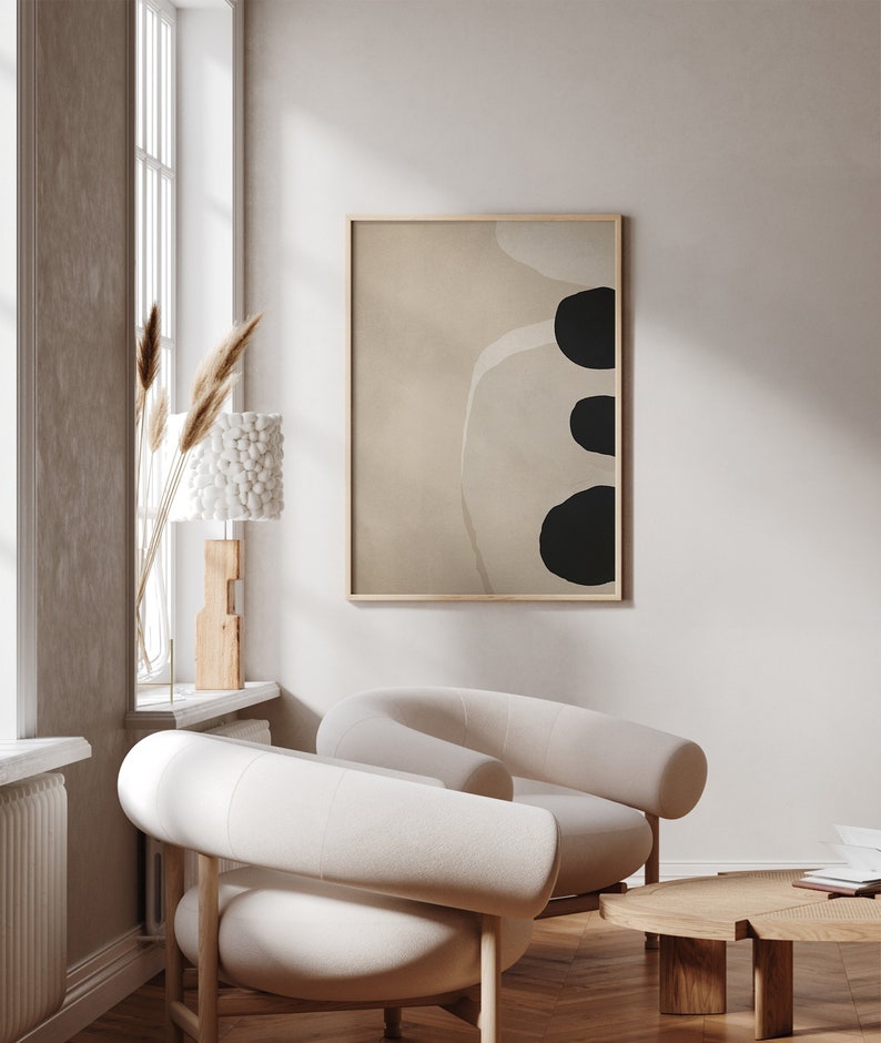 May include: Two white, curved armchairs with wooden legs, a wooden coffee table, and a framed abstract print with black shapes on a beige background.